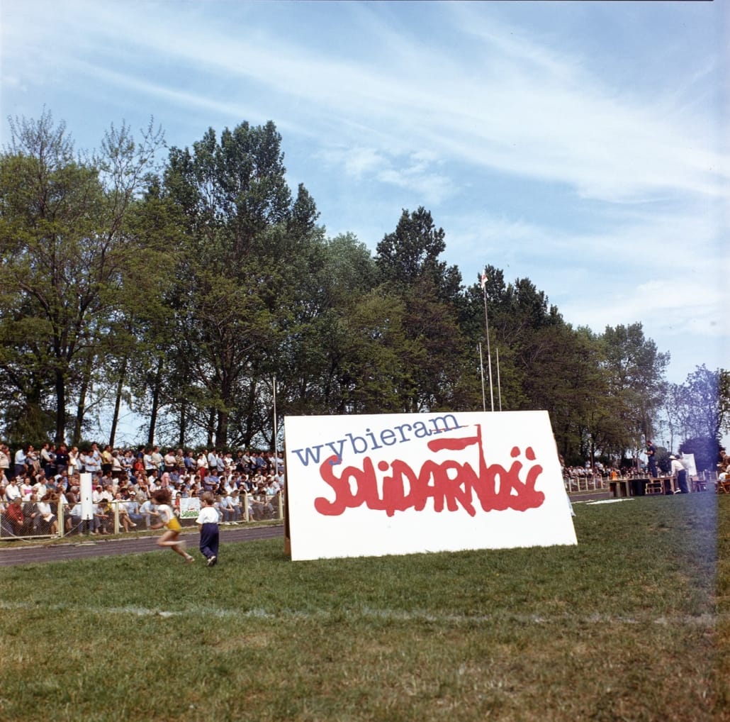 grønn slette/ idrettsarena hvor folk er samlet under en valgkampanje, stor plakat med ordene "Jeg velger Solidaritet" (på polsk). Foto.
